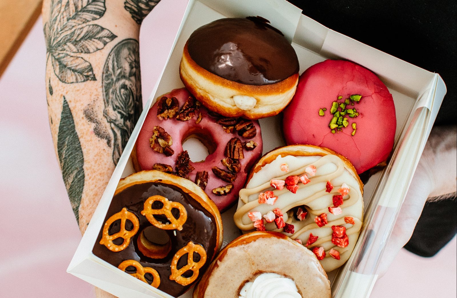 Sechs verschiedene bunte vegane Donuts in einer Kiste, gehalten von tätowierten Armen bei Brammibal's in Berlin Veganuary