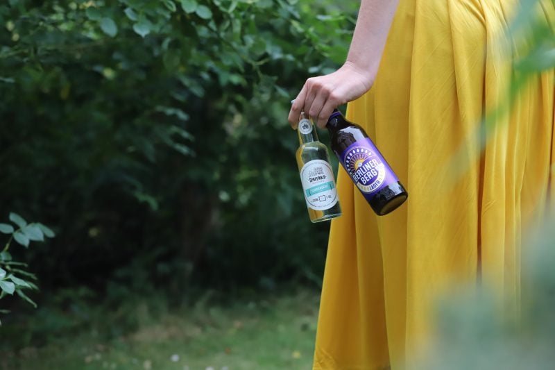 Women in yellow dress walking in the woods with two bottles in her hand.