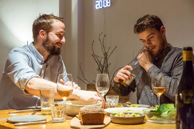 Lode van Zuylen und Stijn Remi am gedeckten Tisch mit Weingläsern und Essen. Sie gehen mit Corona anders um: aus ihrem Fine Dining Restaurant wird ein Gemischtwarenladen.