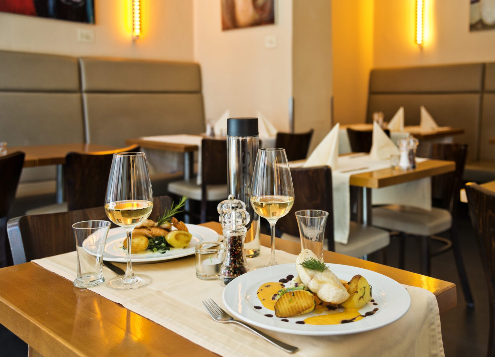 Norwegische Küche? Hat viel zu bieten – zumindest im Munch's Hus.       Skandinavische Küche in Berlin. Zwei Teller auf einem Tisch im Munch's Hus, darauf Fisch und Kartoffeln, zwei Gläser Wein.