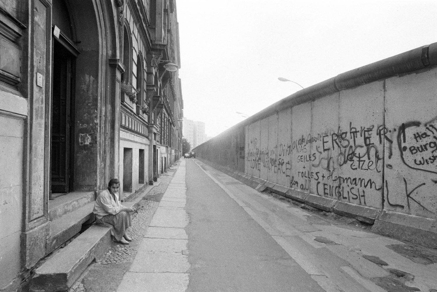 Einsamkeit in Berlin: Türkischstämmiges Mädchen sitzt vor dem Eingang ihres Wohnhauses direkt vor der Berliner Mauer in Kreuzberg, 1984. Foto: Imago/Sommer