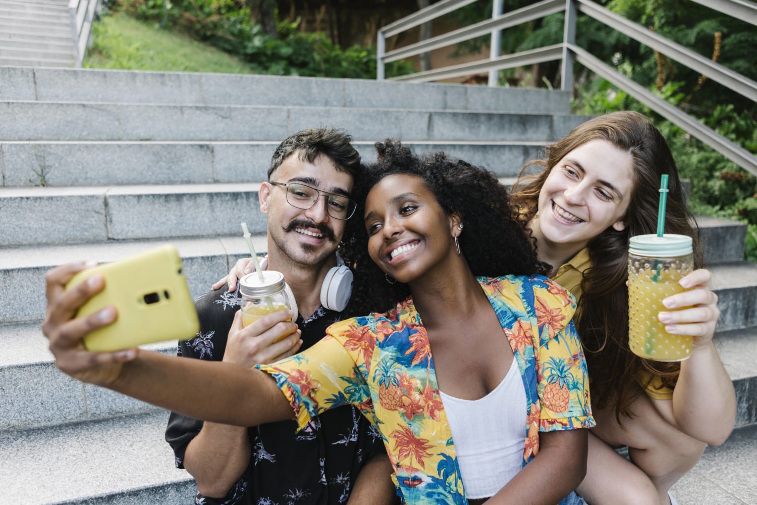 imago images / Westend61 Friends taking selfie on smart phone while sitting in public park model released Symbolfoto XLGF00570