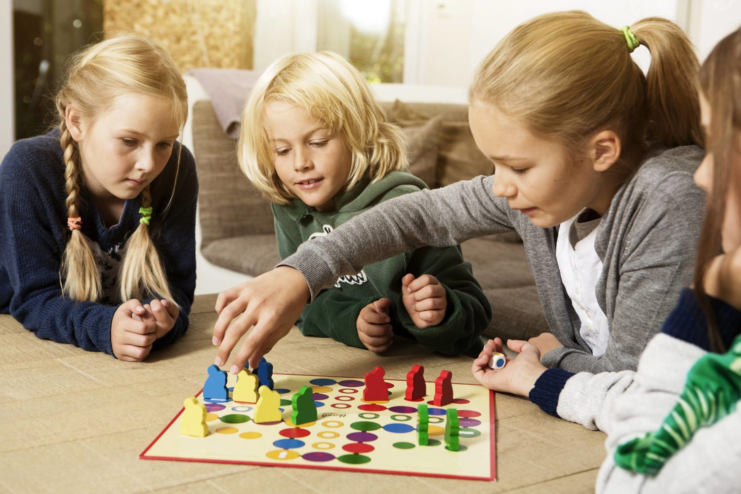 Vier Kinder sitzen auf dem Boden und spielen ein Brettspiel mit bunten Figuren. 