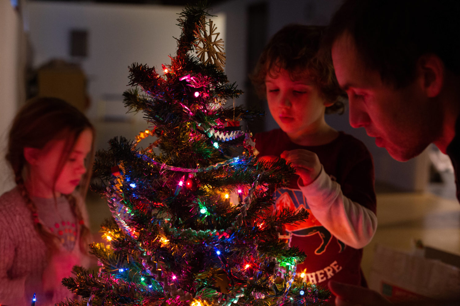 Vater schmückt mit einem kleinen Mädchen und einem Jungen den Weihnachtsbaum.