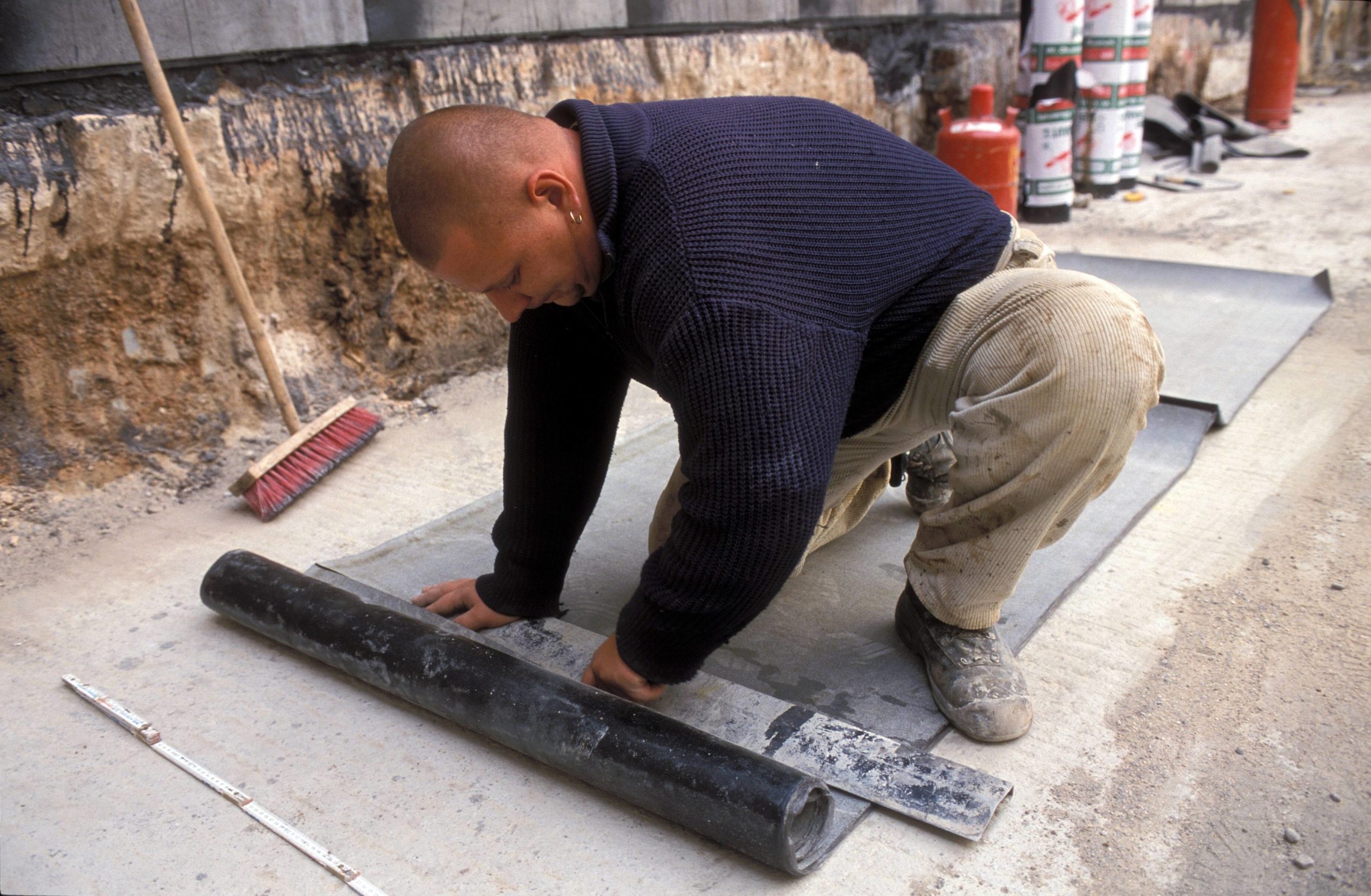 Ein Handwerker schneidet Endlos-Dachpappe zu, eine der vielen Erfindungen aus Brandenburg. Foto: Imago/Günter Schneider
