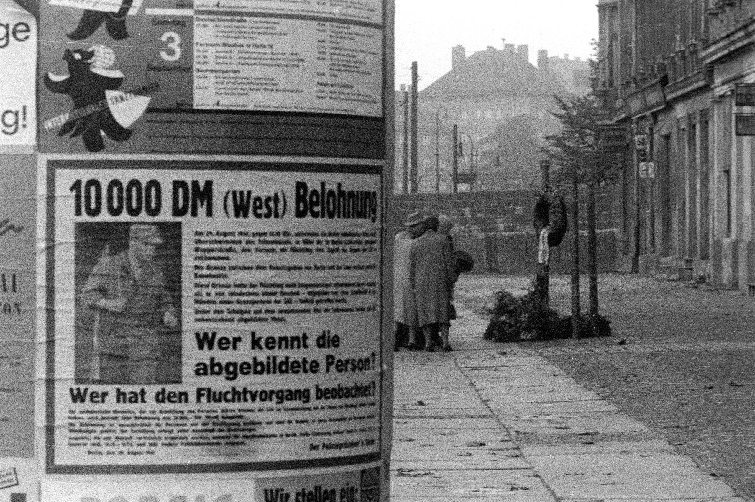 Fahndungsplakat an einer Litfaßsäule vor der Berliner Mauer an der Bernauer Straße, 1961. Foto: Imago/Sabine Gudath