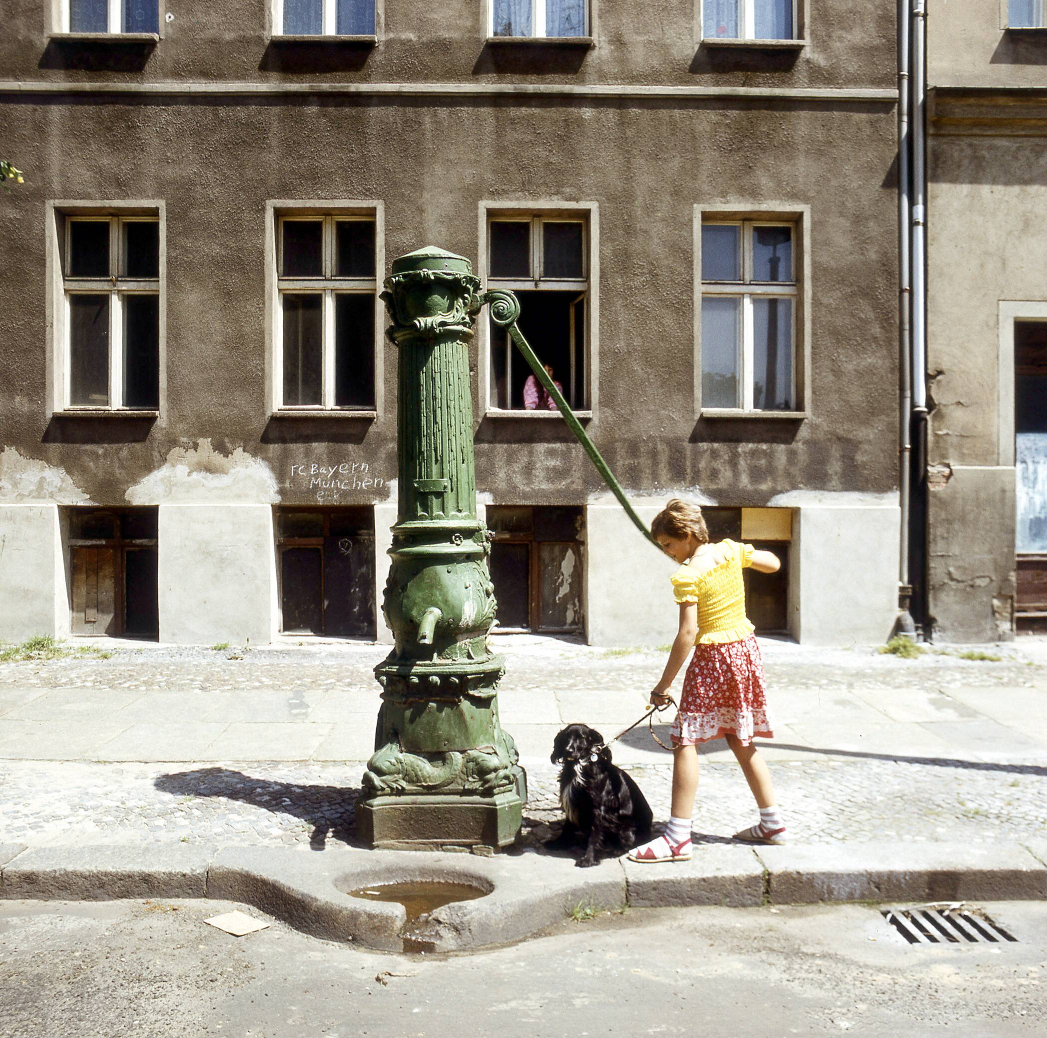 Hunde in Ost-Berlin: Kind mit Hund an einer Wasserpumpe am Arkonaplatz in Prenzlauer Berg, 1976. Foto: Imago/NBL Bildarchiv