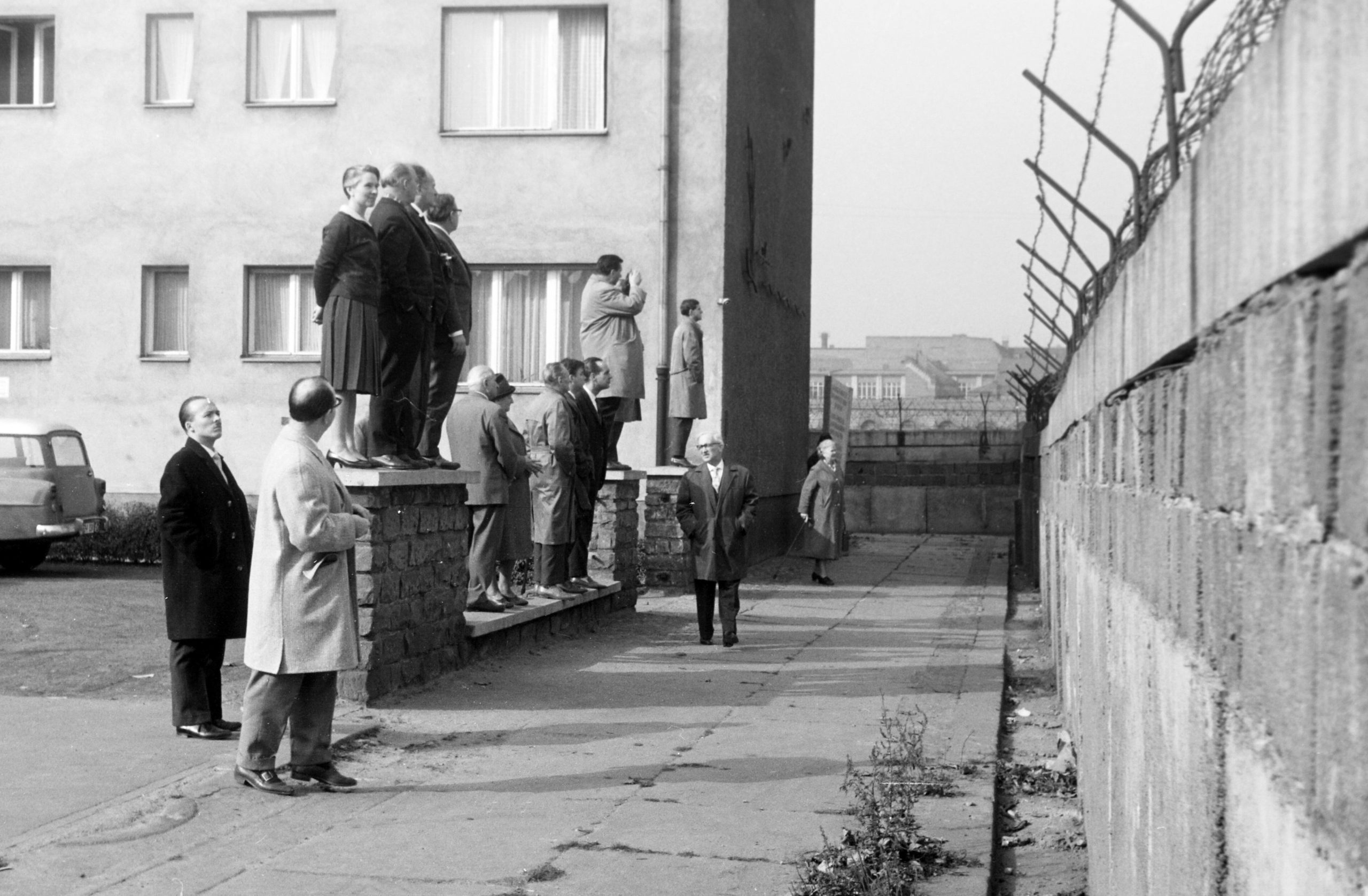 Eine Reisegruppe schaut von einer Vorgartenmauer über die Mauer hinweg vom Westteil in den Ostteil. Foto: Imago/Erich Andres/United Archives
